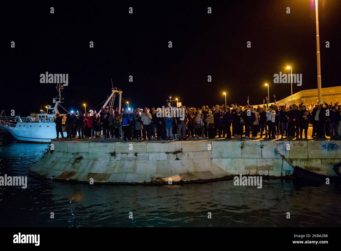People observe the fishing boats in the Port of Molfetta, on the occasion of the 25th anniversary of the disappearance of the fishing boat Francesco Padre with its crew, in Molfetta, Italy, on November 4, 2019. On 4 November 1994, the trawler Francesco Padre exploded off the coast of Montenegro with all his human cargo. That night Giovanni Pansini, Saverio Gadaleta, Luigi De Giglio, Francesco Zaza and Mario De Nicolo lost their lives. To remember them on the evening of November 4th, relatives met in church, but also fellow fishermen, representatives of fishermen's associations, the mayor, Tomm Stock Photo
