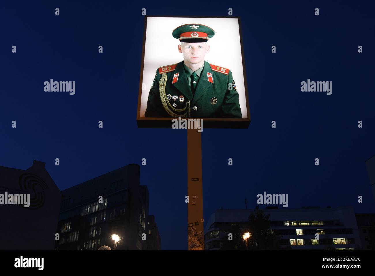 A portrait of a Russian soldier stands illuminated at former Checkpoint Charlie, where U.S. and Soviet tanks confronted each other in the early years of the Cold War, seen just two days ahead of the upcoming 30th anniversary of the fall of the Berlin Wall. The Berlin Wall divided the German capital from 1961 until 1989. Checkpoint Charlie was a main crossing point at the Wall from the American Sector in West Berlin into the Russian sector in East Berlin. On Thursday, November 7, 2019, in Berlin, Germany. (Photo by Artur Widak/NurPhoto) Stock Photo