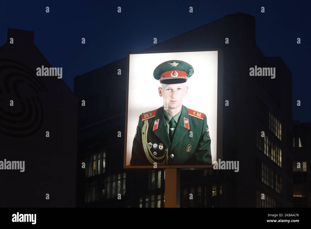 A portrait of a Russian soldier stands illuminated at former Checkpoint Charlie, where U.S. and Soviet tanks confronted each other in the early years of the Cold War, seen just two days ahead of the upcoming 30th anniversary of the fall of the Berlin Wall. The Berlin Wall divided the German capital from 1961 until 1989. Checkpoint Charlie was a main crossing point at the Wall from the American Sector in West Berlin into the Russian sector in East Berlin. On Thursday, November 7, 2019, in Berlin, Germany. (Photo by Artur Widak/NurPhoto) Stock Photo
