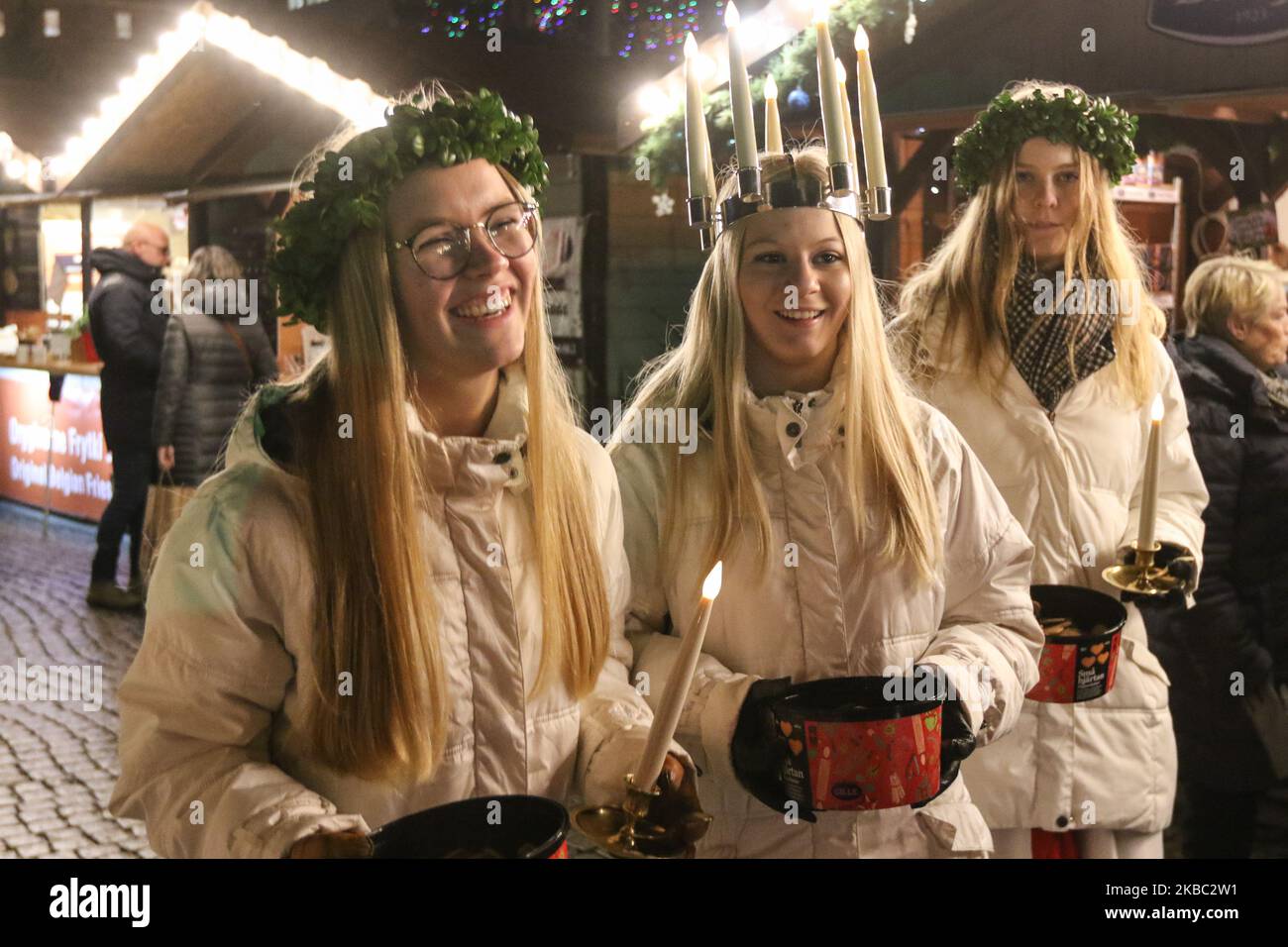 Young girls from Kalmar, Sweden dressed in a white dress and a red sash (as the symbol of martyrdom) carries candles in proccesion along the Gdansk Christmas Fair on the Old City centre area are seen in Gdansk, Poland on 2 December 2019 . One of them wears a crown of candles on her head. Girls dressed as Saint Lucy (Sankta Lucia) carry cookies in procession and sing a songs. It is said that to vividly celebrate St. Lucy's Day will help one live the long winter days with enough light. (Photo by Michal Fludra/NurPhoto) Stock Photo