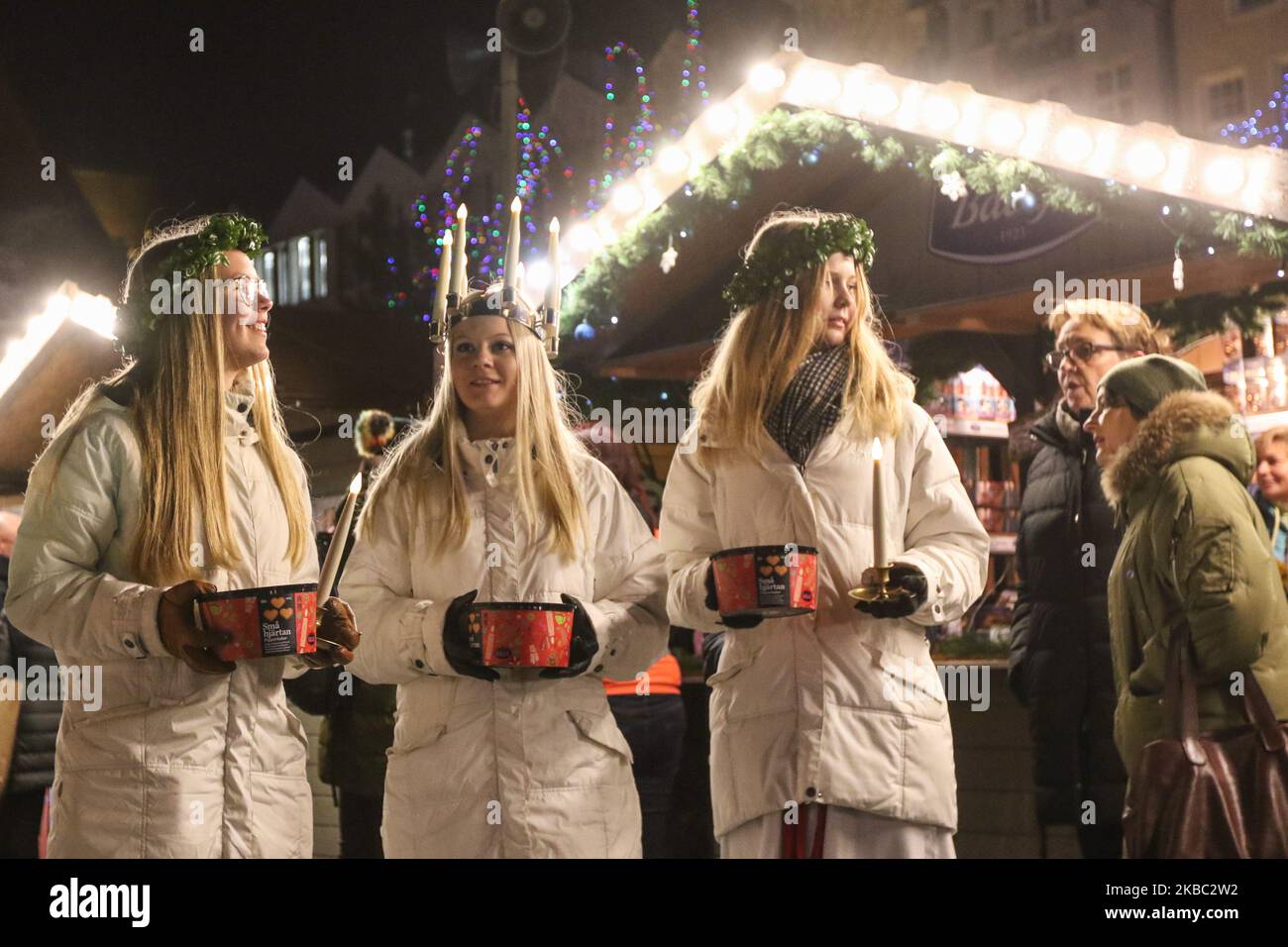 Young girls from Kalmar, Sweden dressed in a white dress and a red sash (as the symbol of martyrdom) carries candles in proccesion along the Gdansk Christmas Fair on the Old City centre area are seen in Gdansk, Poland on 2 December 2019 . One of them wears a crown of candles on her head. Girls dressed as Saint Lucy (Sankta Lucia) carry cookies in procession and sing a songs. It is said that to vividly celebrate St. Lucy's Day will help one live the long winter days with enough light. (Photo by Michal Fludra/NurPhoto) Stock Photo