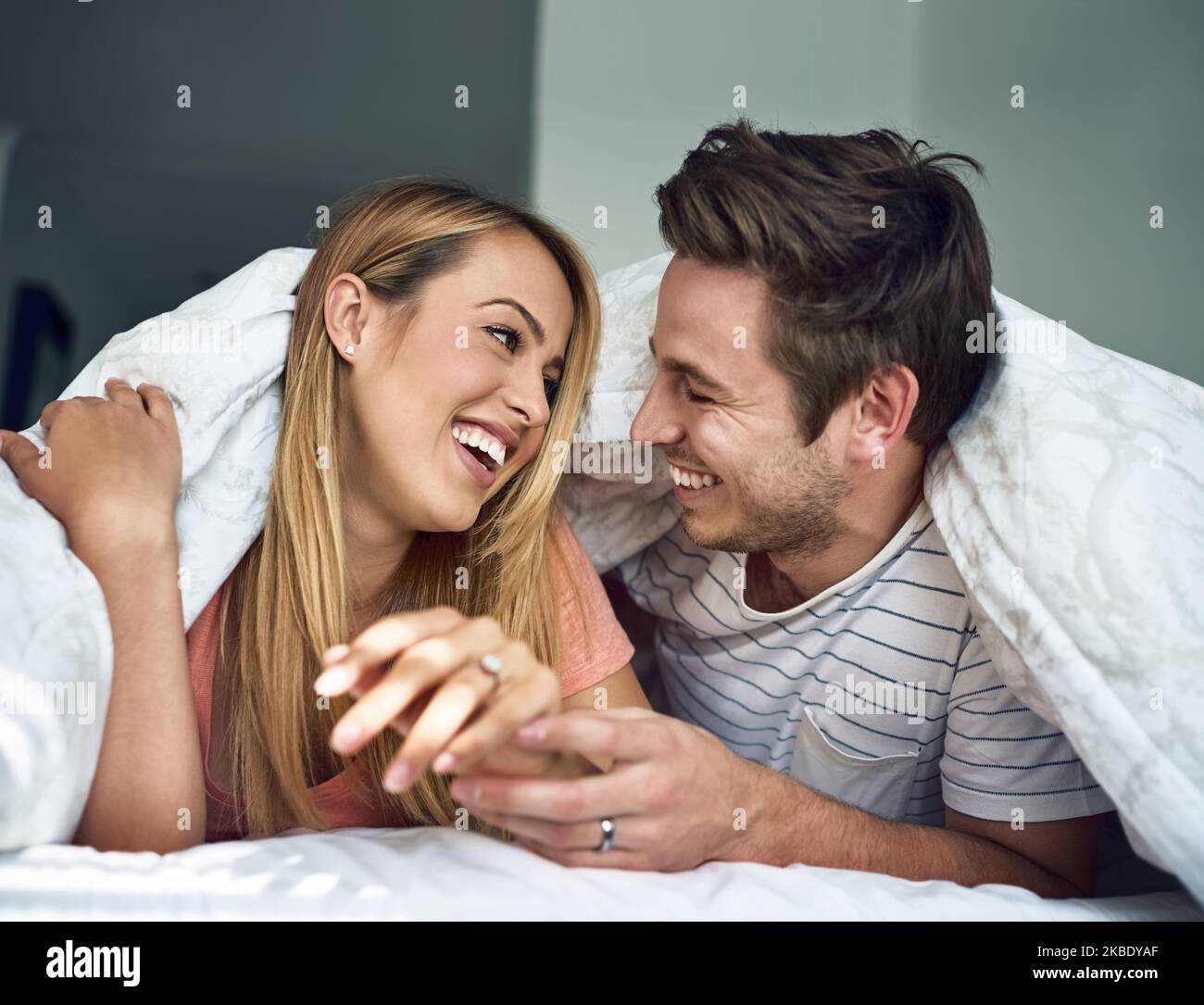 Your happy makes me happy. a happy young couple relaxing under a duvet together in bed. Stock Photo