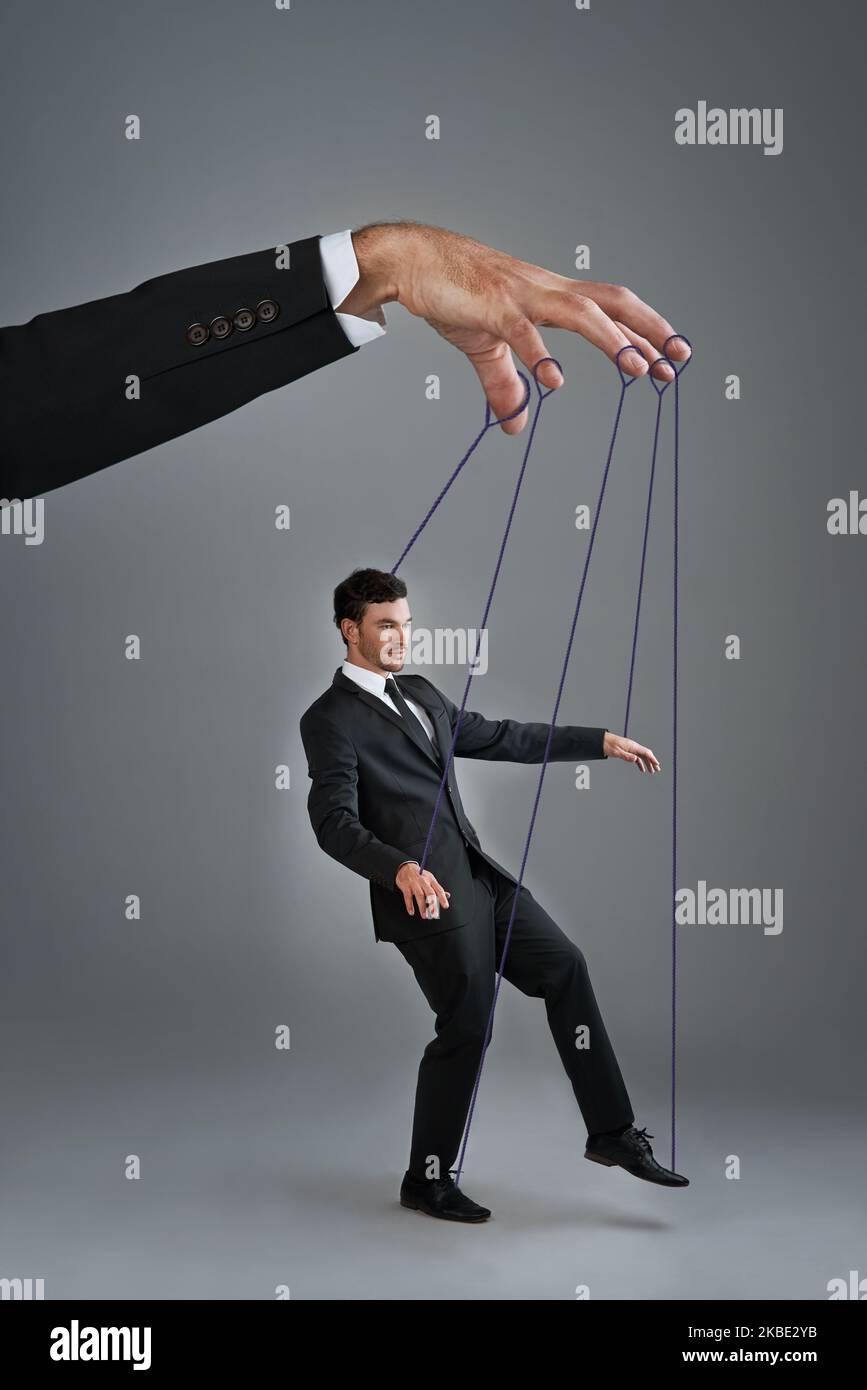 If you dont control your business, someone else will. Studio shot of a young businessman being controlled like a puppet by a giant hand against a gray Stock Photo