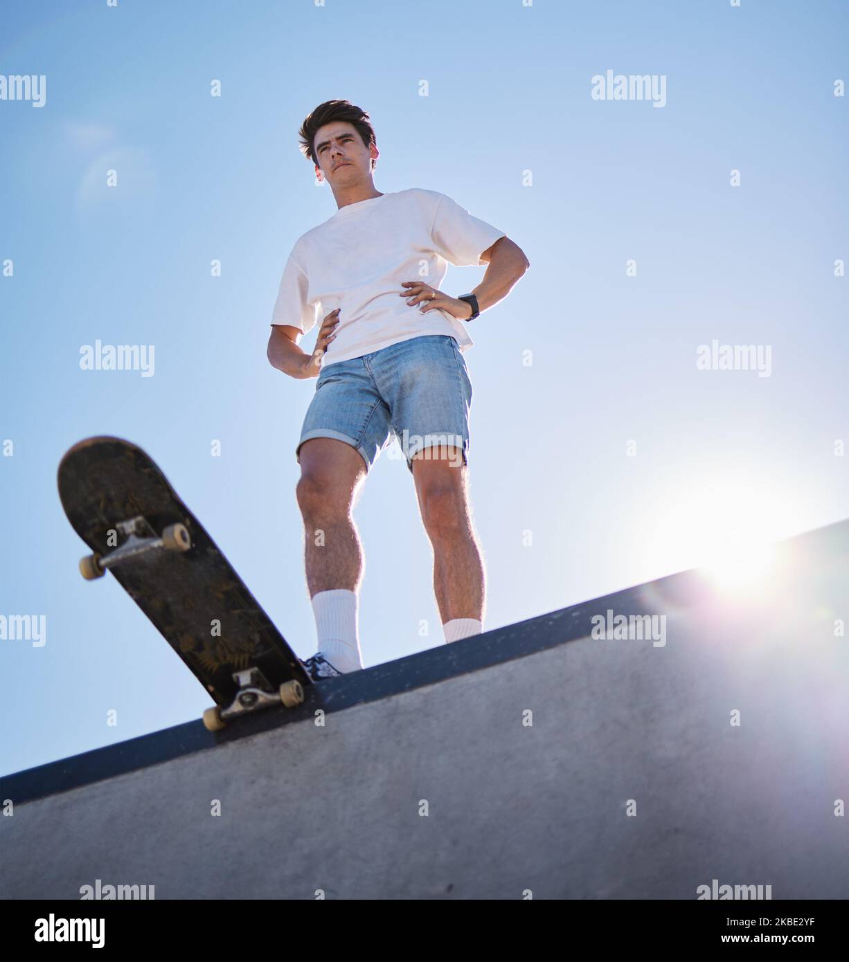 Blue sky, skateboard and young man from below on skate ramp ready for ...