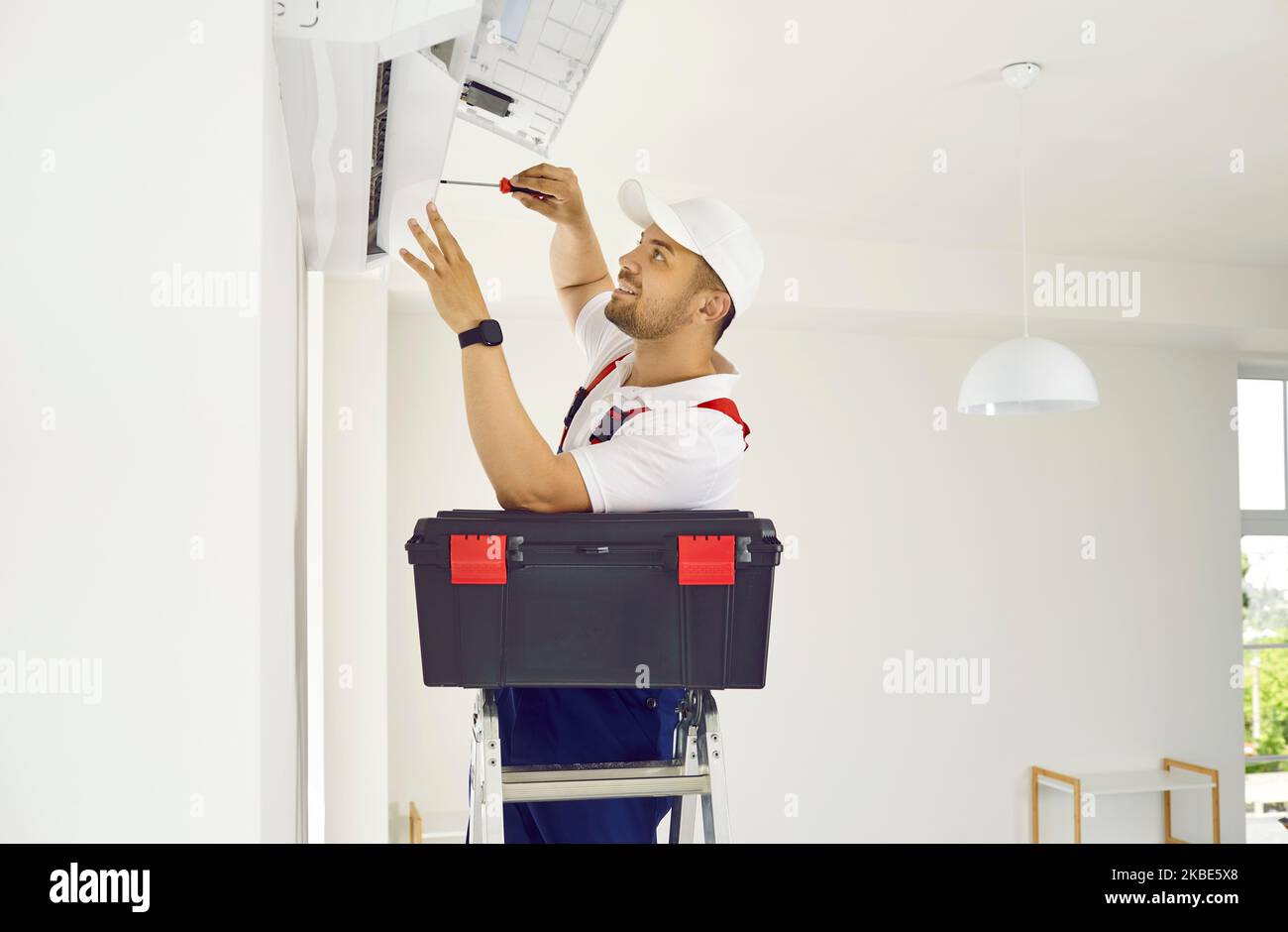 Worker with toolbox standing on ladder and installing modern air conditioner on wall Stock Photo