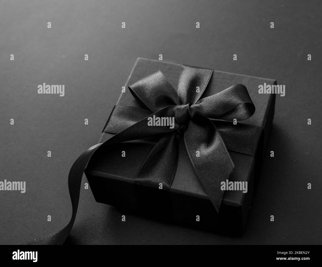 Black Friday Sale and Christmas presents concept. Gift box with black ribbon on red satin textile, close up view Stock Photo