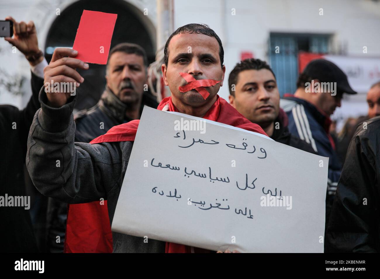 A man with a mouth taped shut holds a placard which reads in Arabic, 'Red card to all politicians who aimed to destruct Tunisia', he also shows a red card as a warning against the government as he attends the gathering held outside the UGTT labor union headquarters in Tunis to celebrate the 9th anniversary of the revolution which drove former president Zine El-Abidine Ben Ali away on 15 January 2020 in Tunis, Tunisia. (Photo by Chedly Ben Ibrahim/NurPhoto) Stock Photo