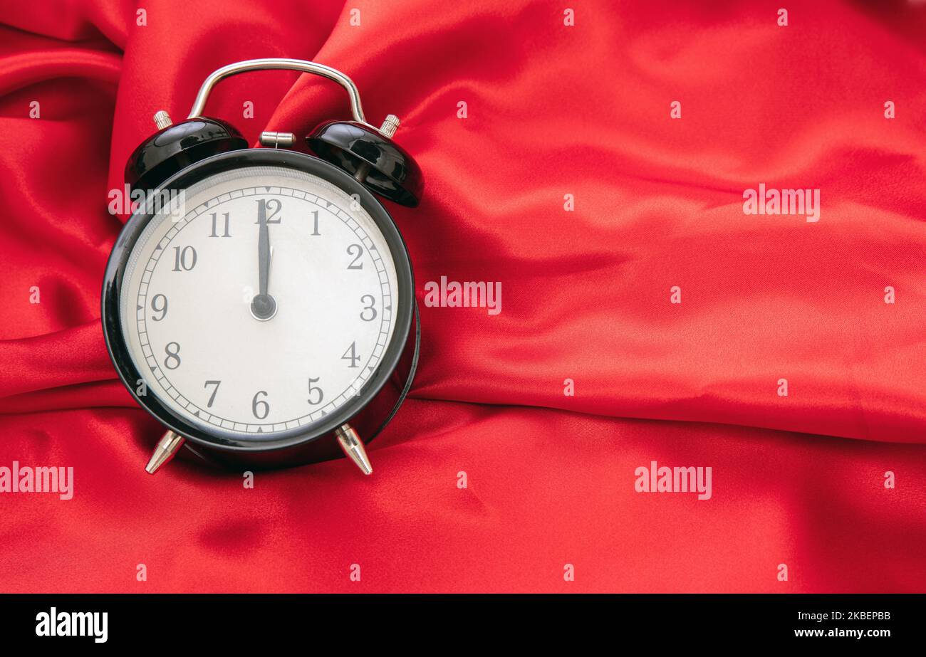 Black retro alarm clock on red satin background top view, copy space. Stock Photo