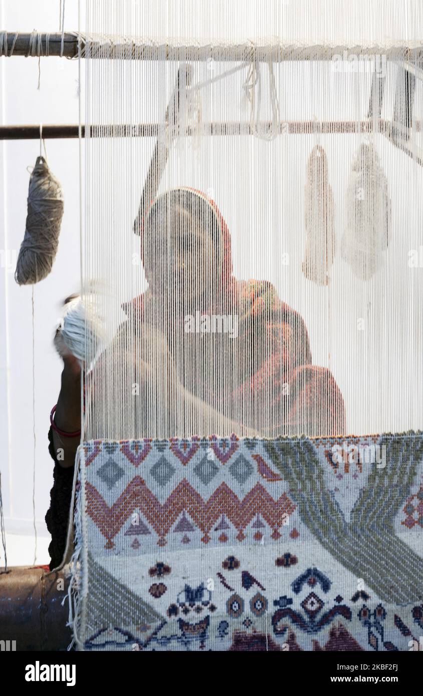 A woman artisan hand knotts a carpet on the loom at the stand of Jaipur ...
