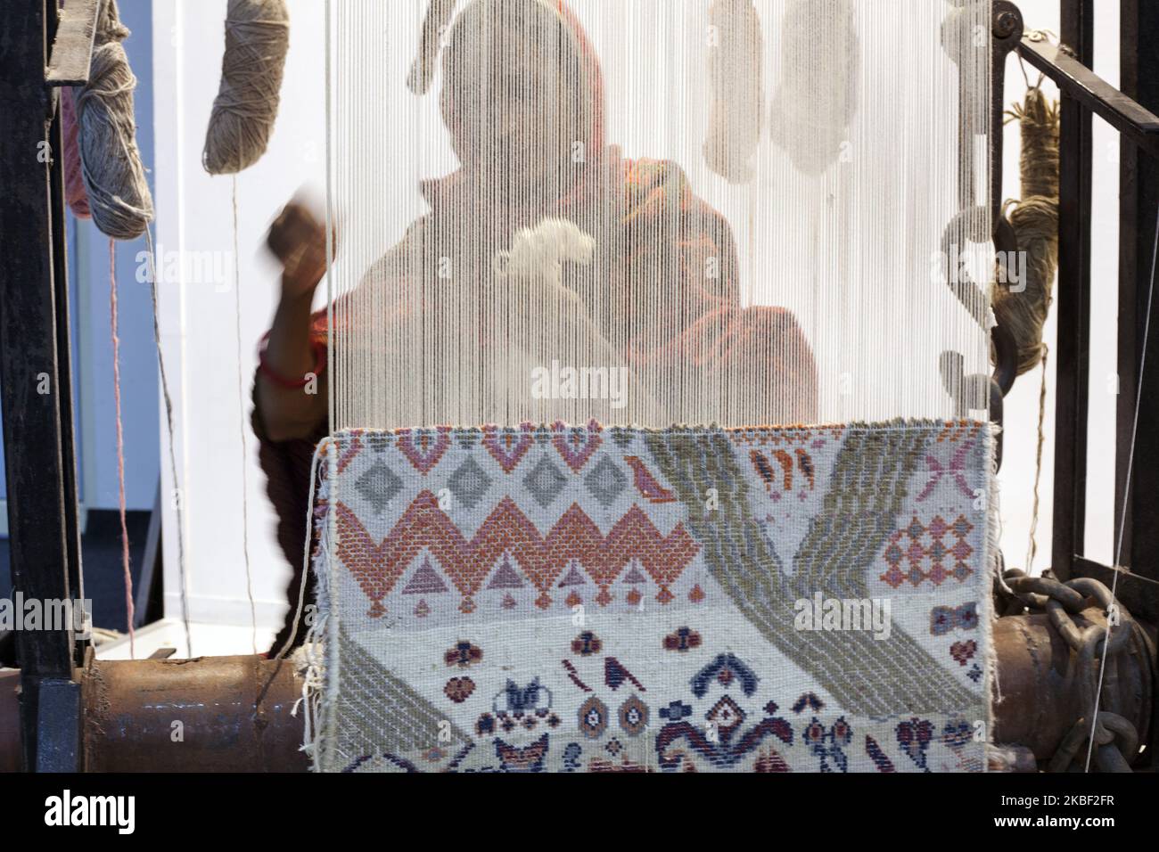 A woman artisan hand knotts a carpet on the loom at the stand of Jaipur ...