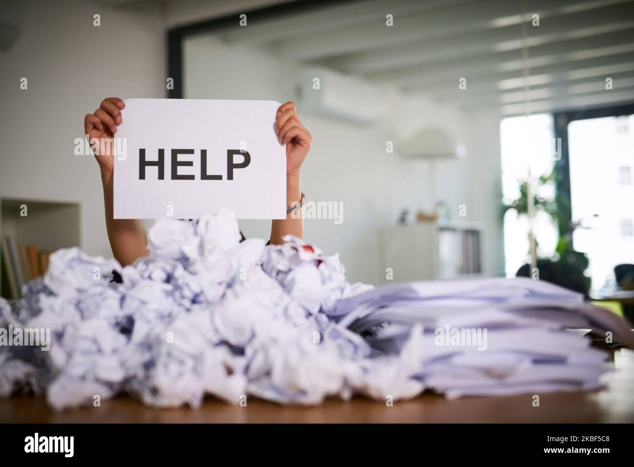 Dont let admin be your downfall. an unidentifiable businesswoman holding up a sign that reads help while drowning under a pile of paperwork in the Stock Photo