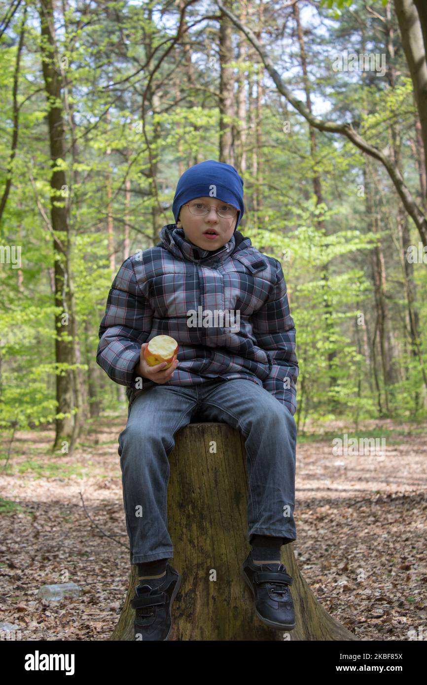 emotion of a surprised boy sitting on a stump in the forest Stock Photo
