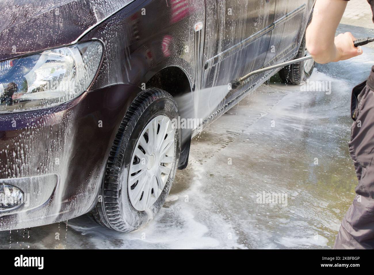 Man, washing his car Wheels of a car wash, using a high pressure water