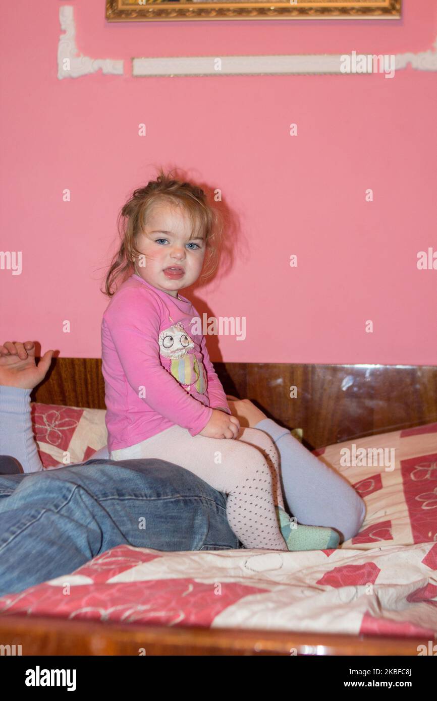 Girl sits on her belly dad on the bed Stock Photo