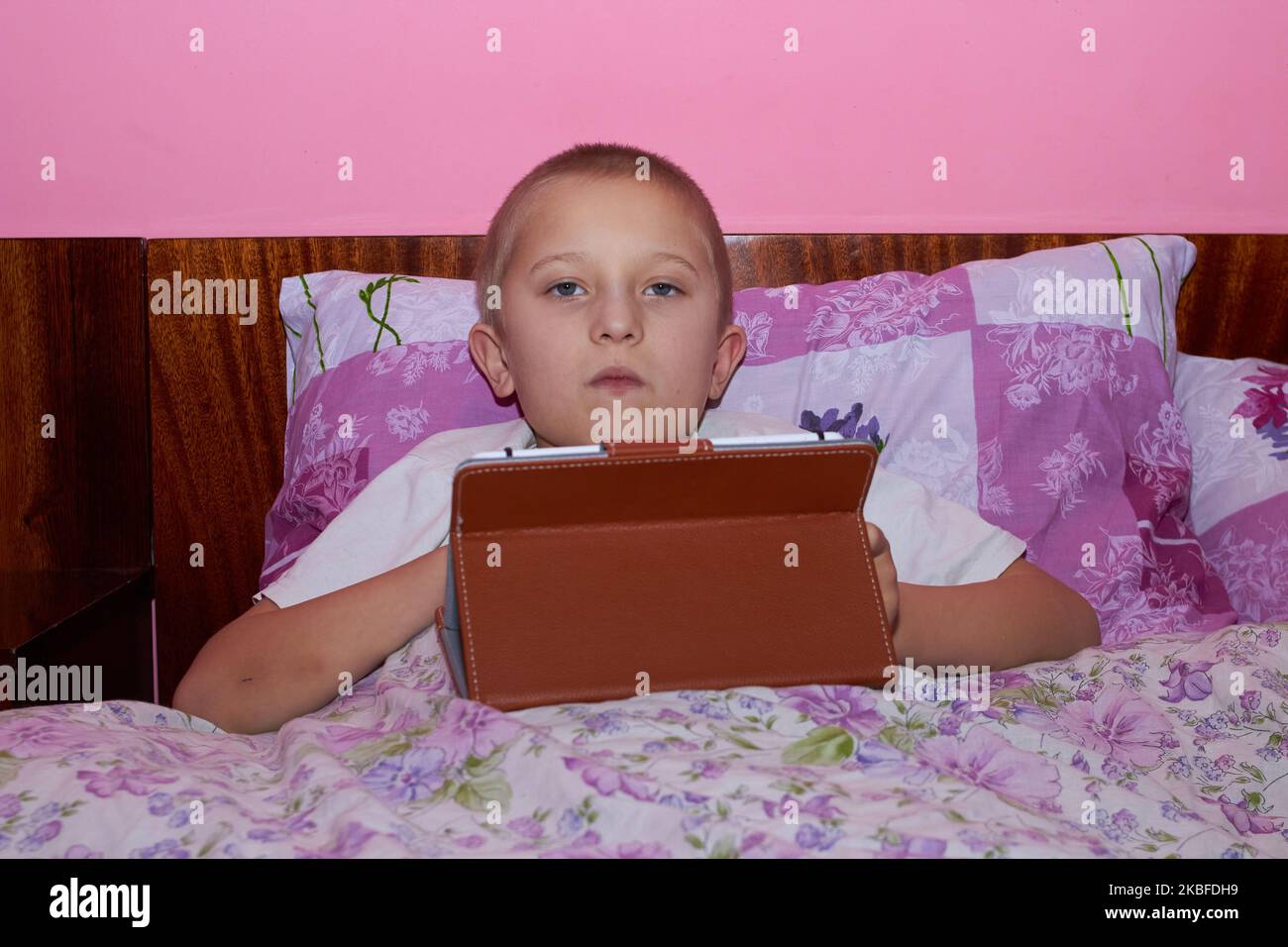 little boy lying in bed with a tablet pc and playing games with friends ...