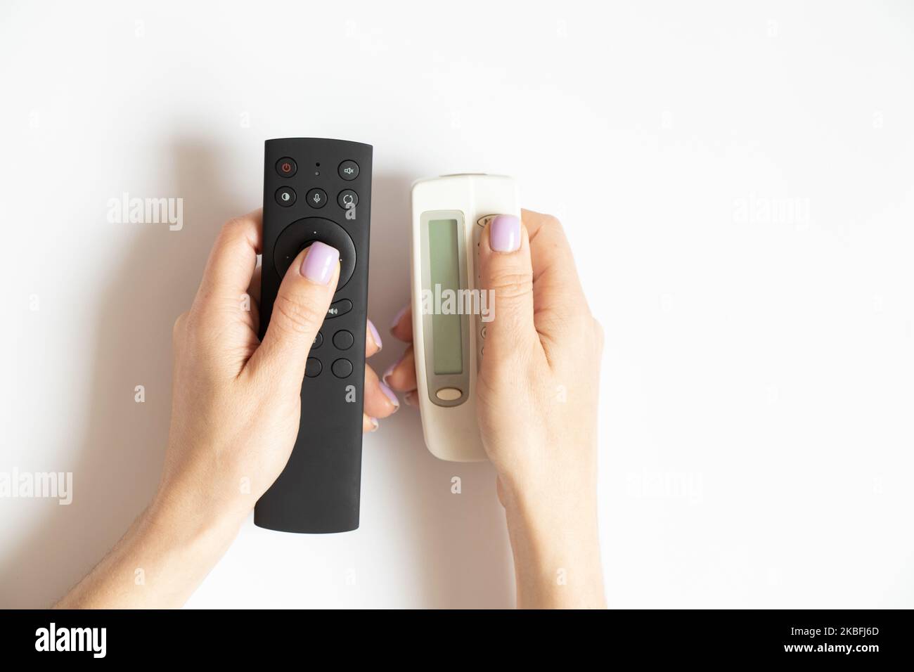Two remote controls in female hands on a white background close-up, TV remote control Stock Photo