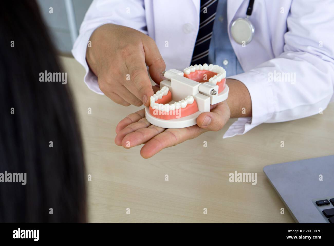Dentist in white gown and stethoscope pointing finger at tooth model