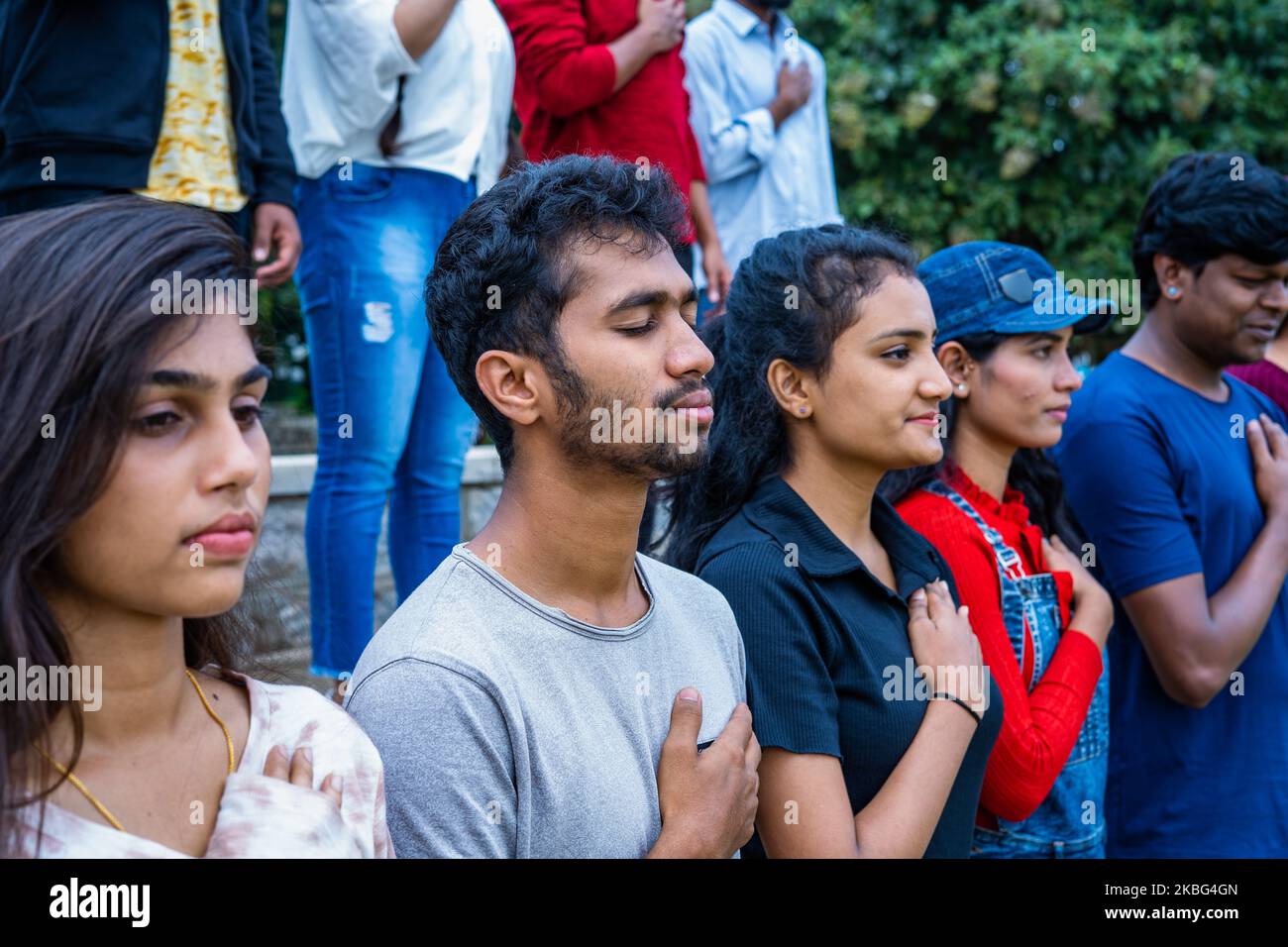 side view medium shot of group of spectators or audience praying or singing national anthem stadium before match - concept of respect, freedom and Stock Photo