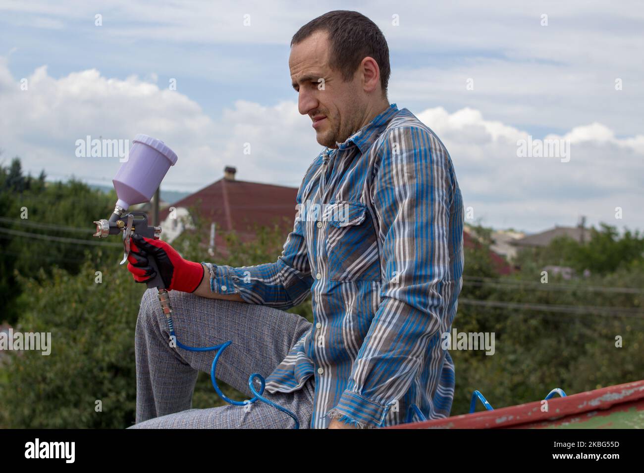 roofer builder worker with pulverizer spraying paint on metal sheet roof Stock Photo