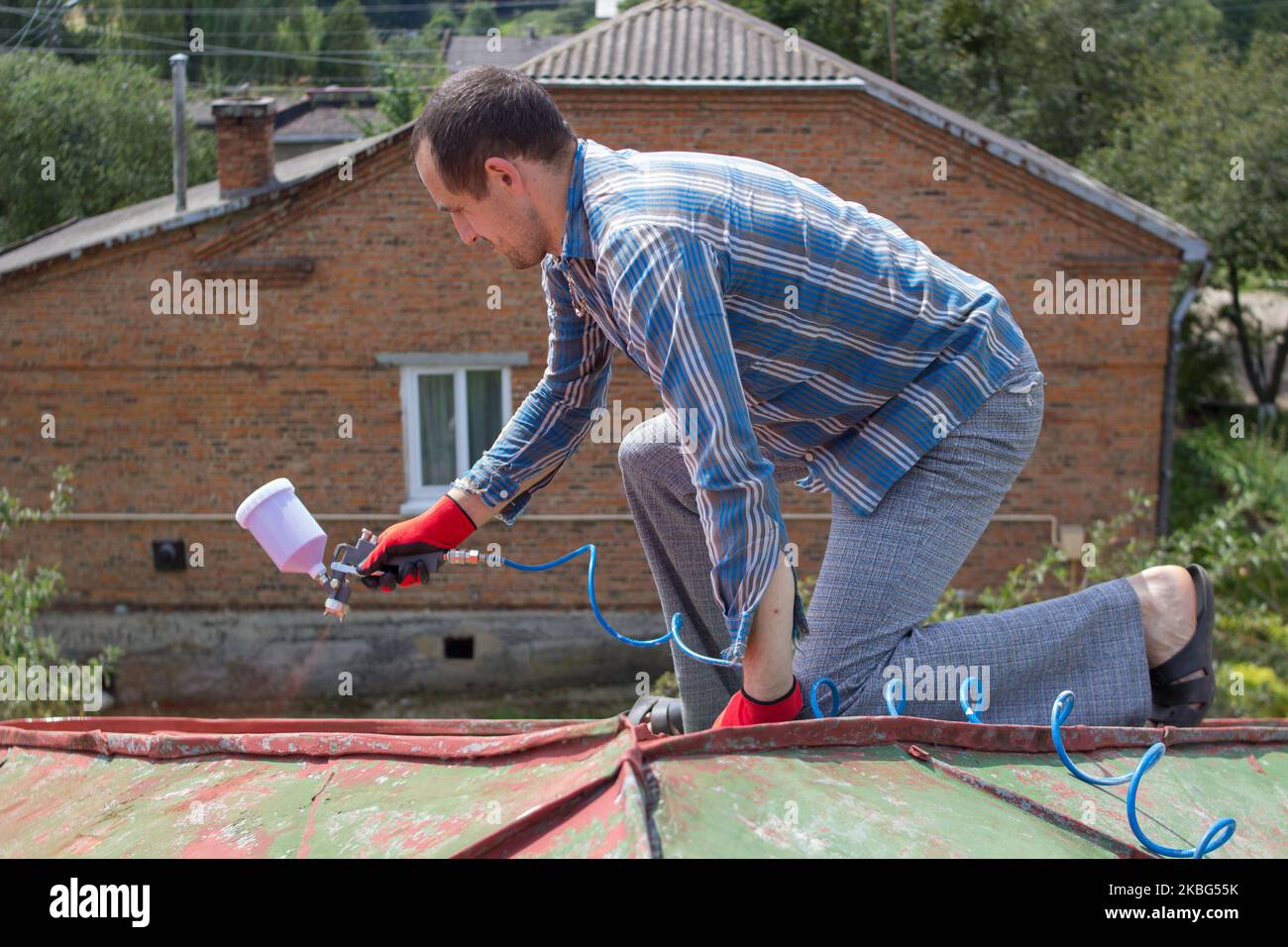 roofer builder worker with pulverizer spraying paint on metal sheet roof Stock Photo