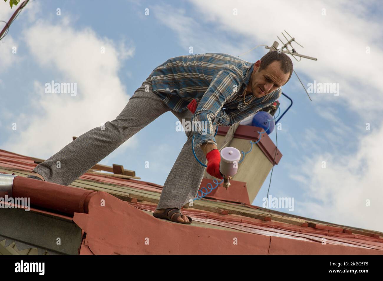 young man on the roof of the house stands and paints the roof Stock Photo