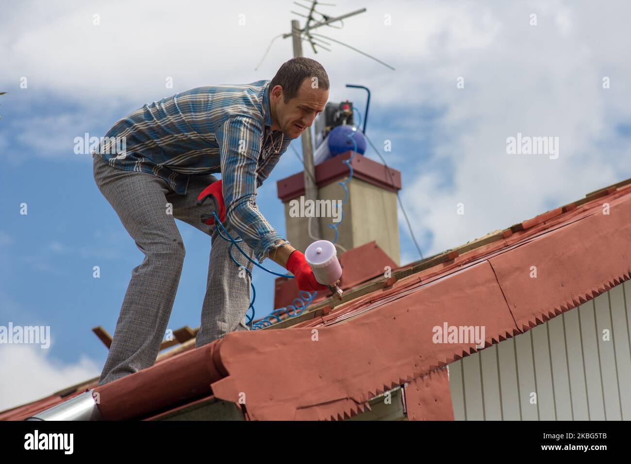 man sprays paint from gun on roof of house in summer Stock Photo