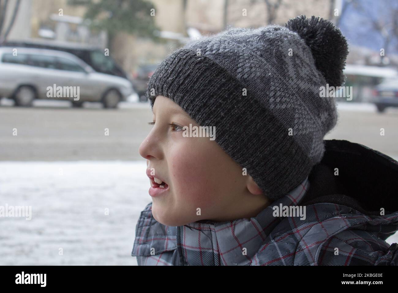 Portrait of a child boy standing by busy road in winter time, road safety concept. Stock Photo