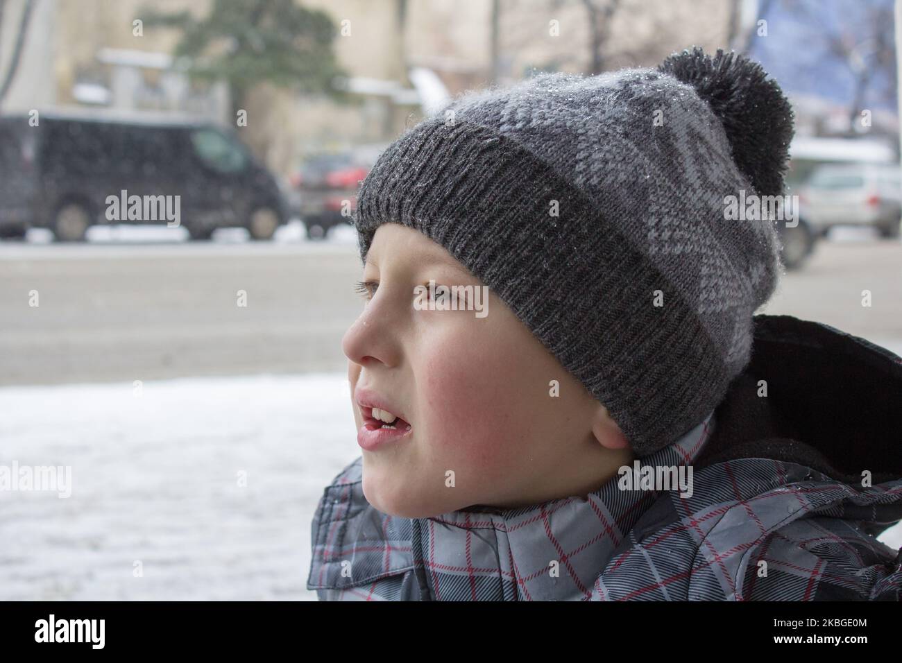 little boy in winter looks to traffic cars on the road Stock Photo
