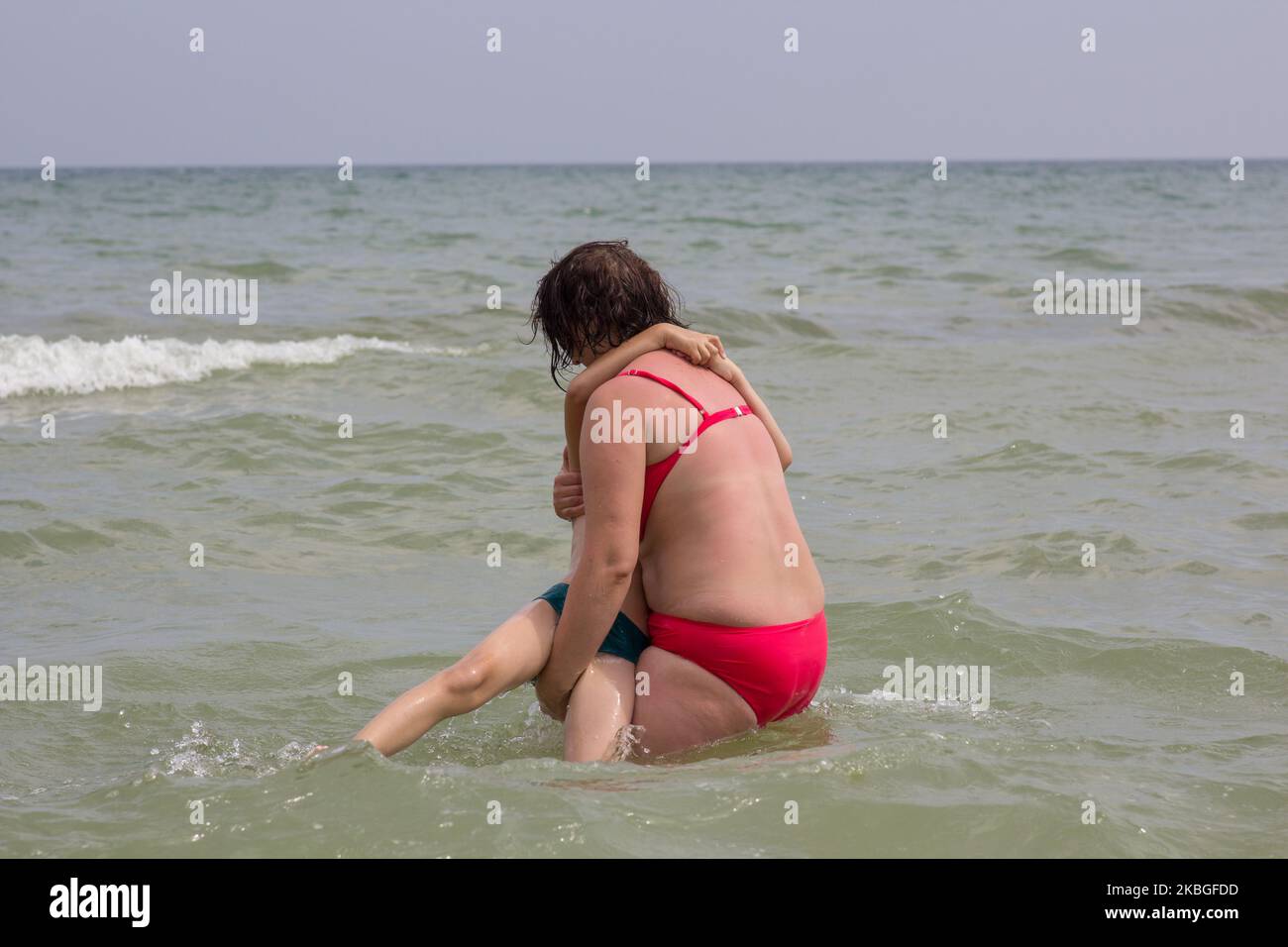 boy is afraid of water in the sea, mom holds on her hands Stock Photo