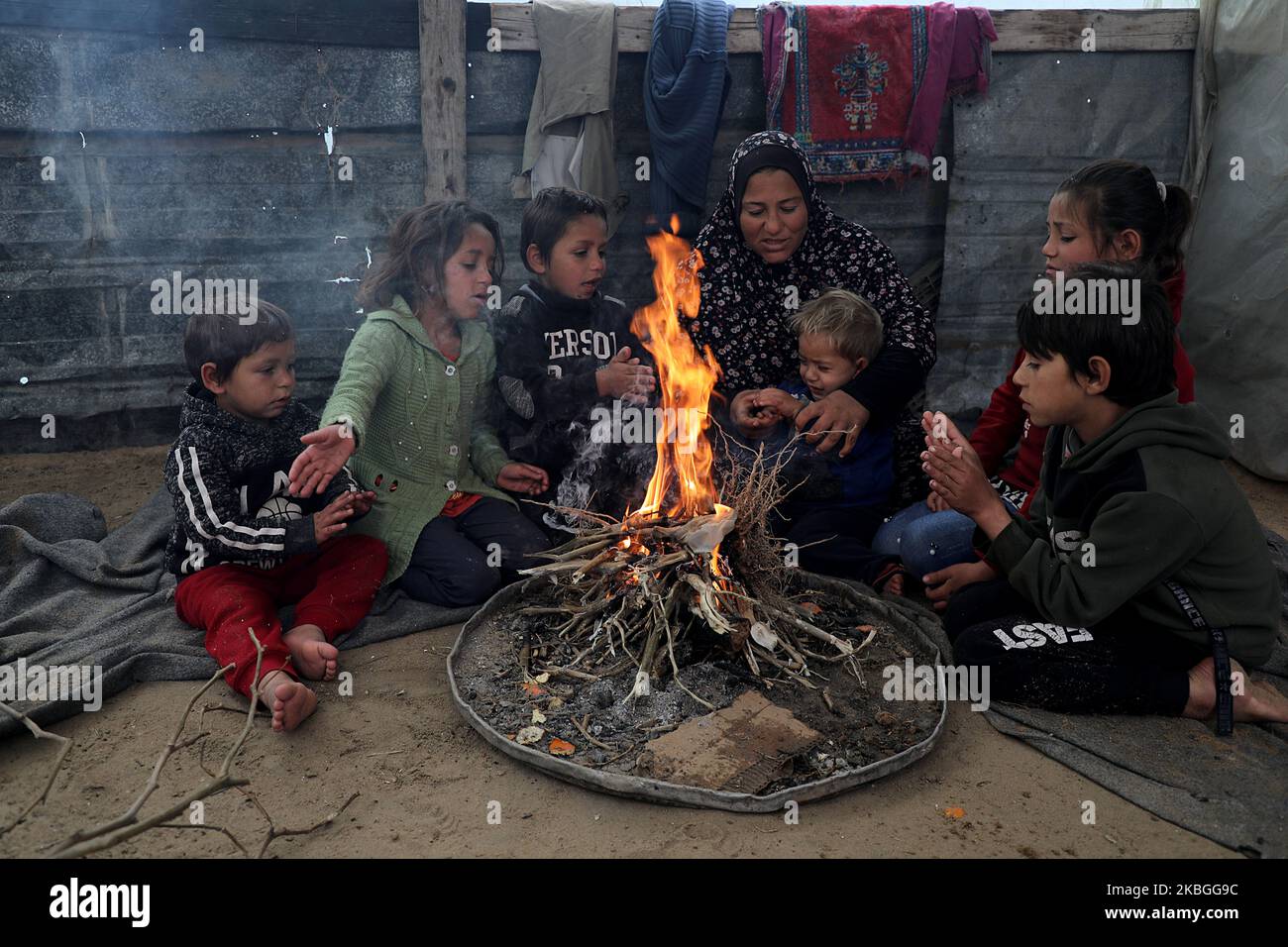 Members of a Palestinian family sit around a fire to warm themselves ...