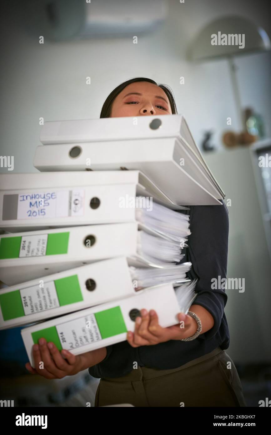 Its going to be a busy day. Portrait of a hardworking businesswoman struggling to carry a heap of files in the office. Stock Photo