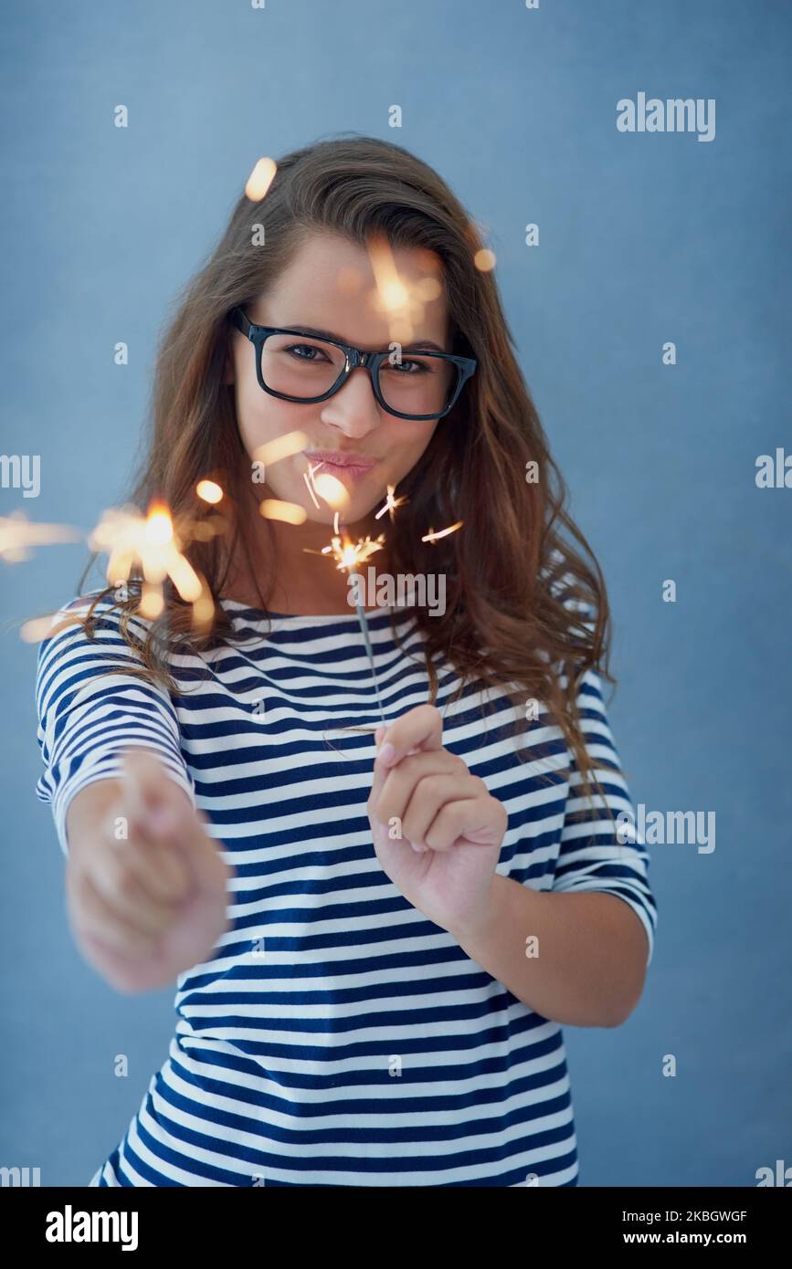 Dont you dare dim your light to make others comfortable. Studio shot of a beautiful young woman holding sparklers against a blue background. Stock Photo