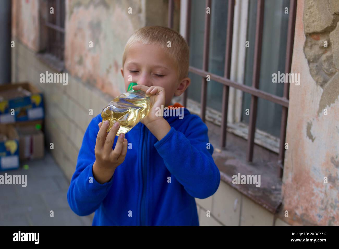 A teen is drinking water from a bottle in the street near the window Stock Photo