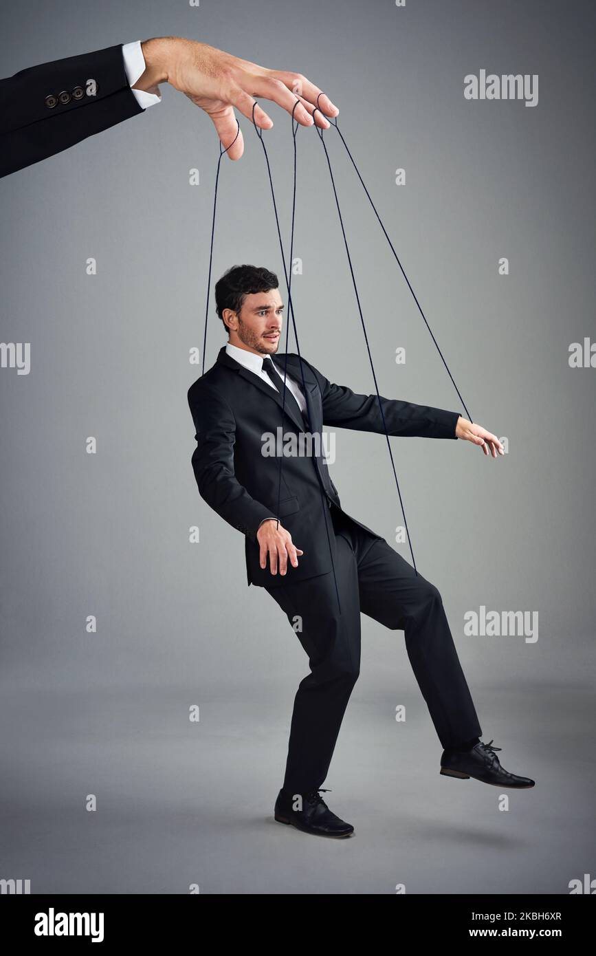 If you dont control your business, someone else will. Studio shot of a young businessman being controlled like a puppet by a giant hand against a gray Stock Photo