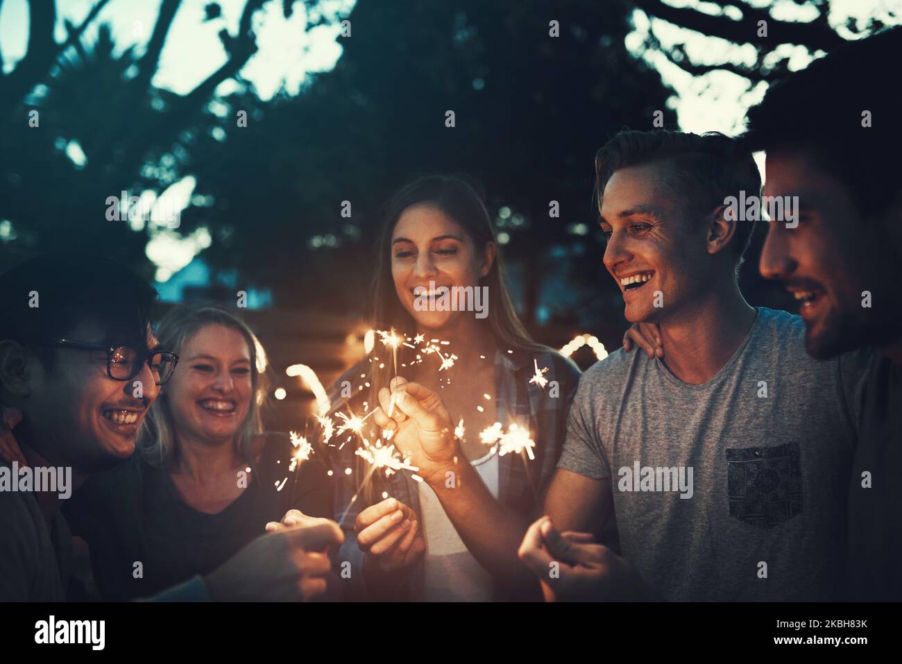 Unforgettable moments with the squad. a group of cheerful young friends having fun with sparklers together outside in the evening. Stock Photo