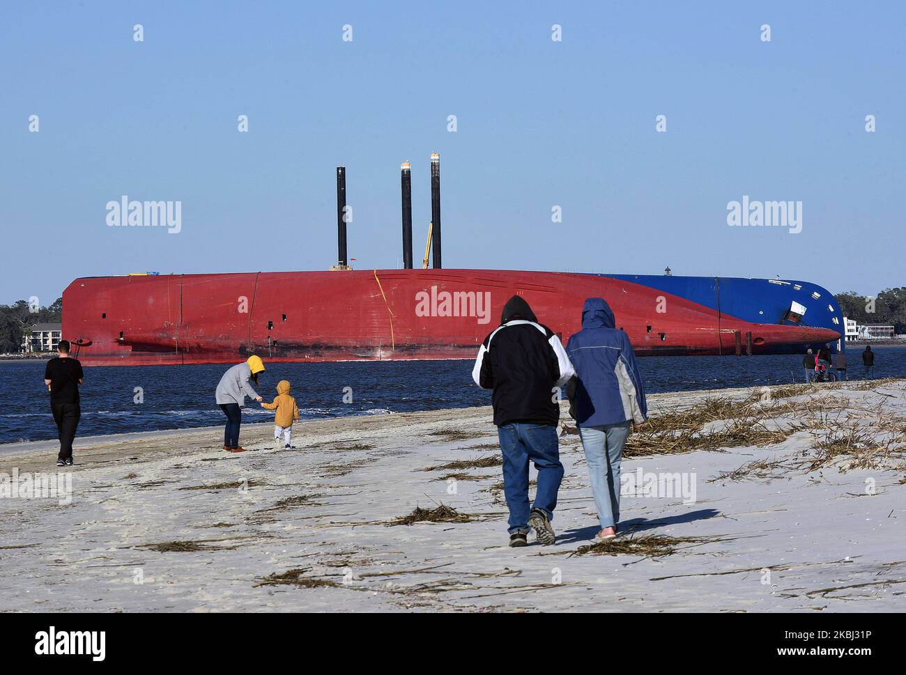 People walk the beach near the Golden Ray cargo ship on February 27
