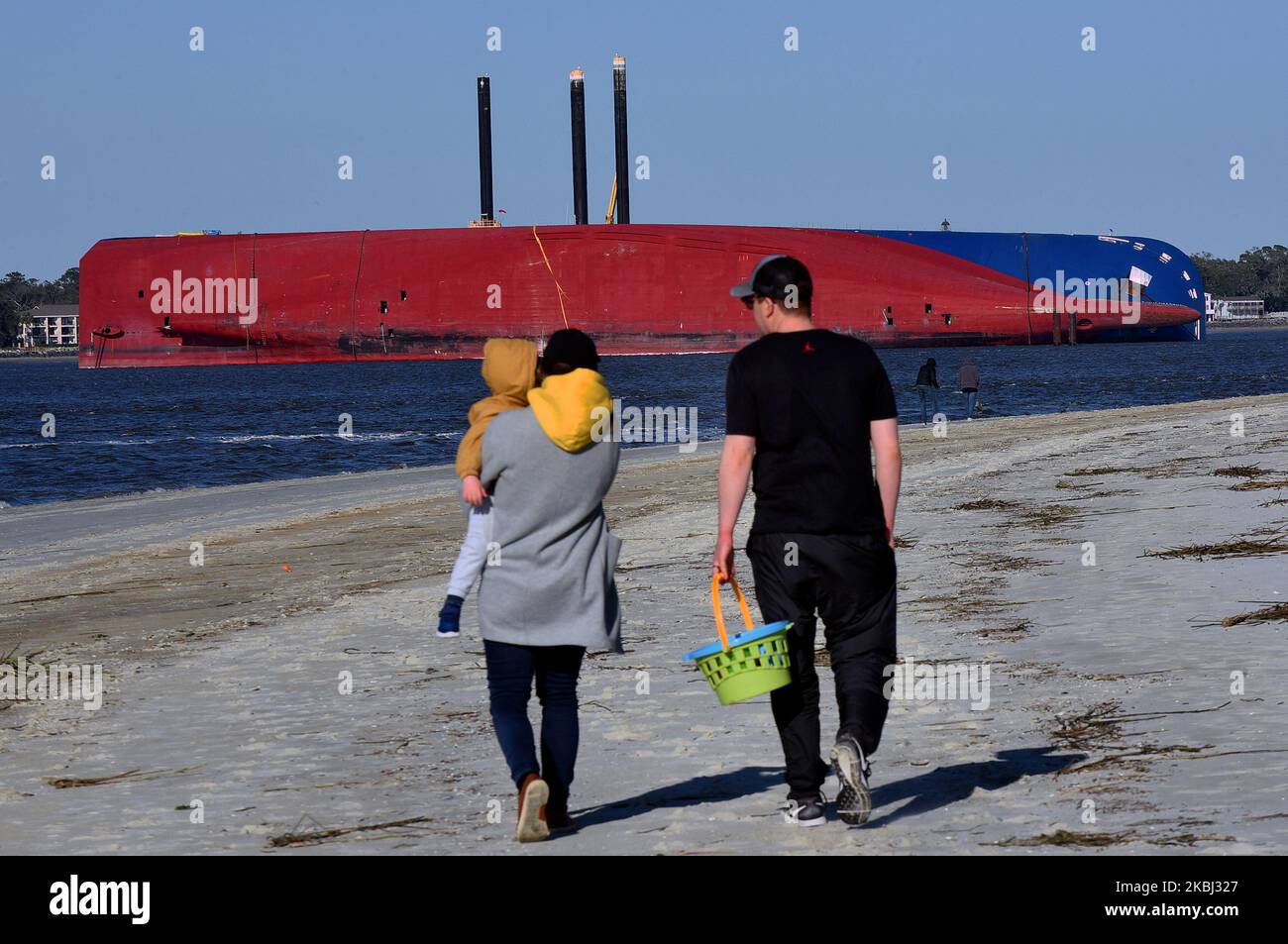 People walk the beach near the Golden Ray cargo ship on February 27