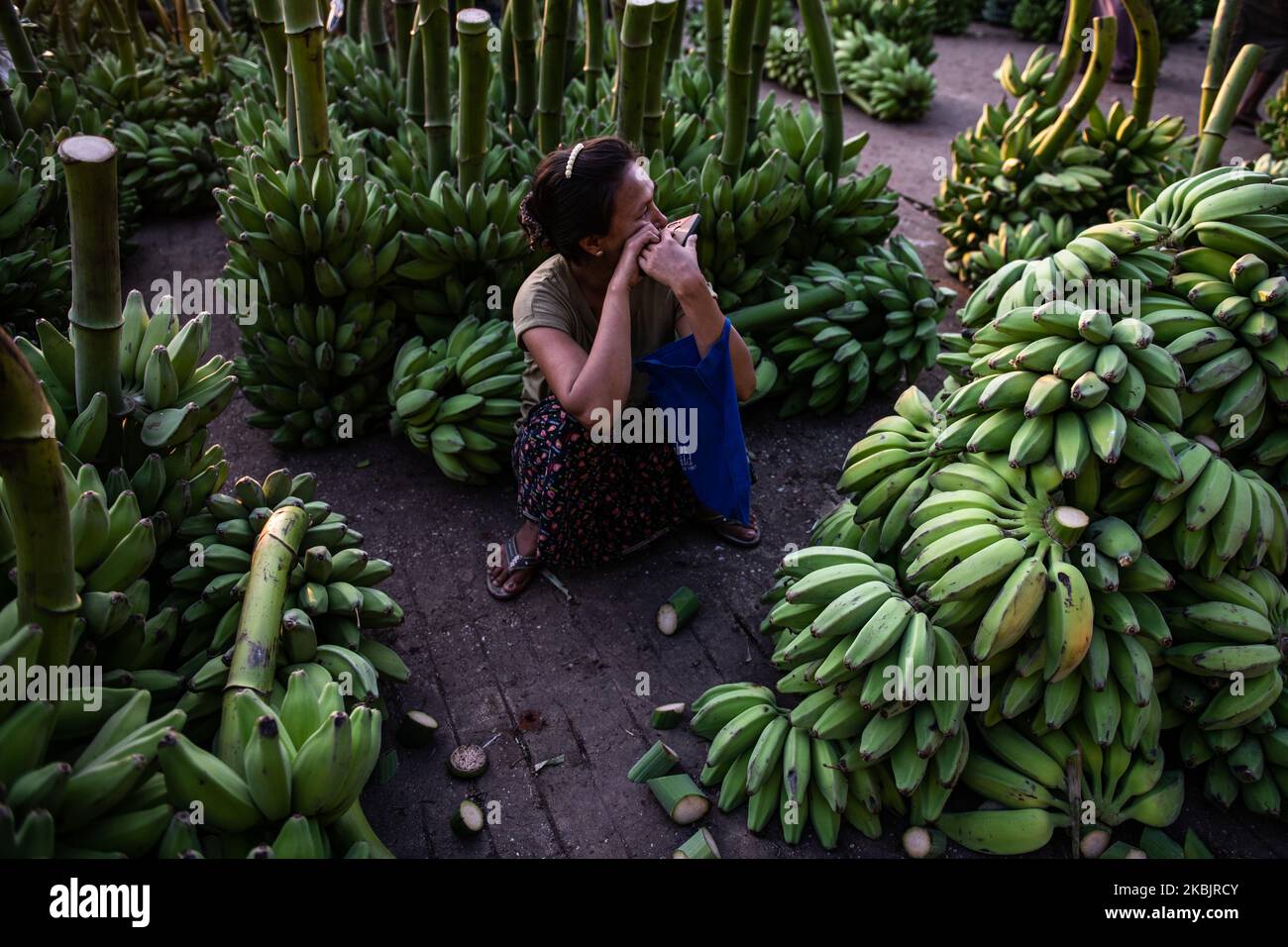 A woman sits near a pile of bananas at a wholesale market in Yangon, Myanmar on March 10, 2020. (Photo by Shwe Paw Mya Tin/NurPhoto) Stock Photo