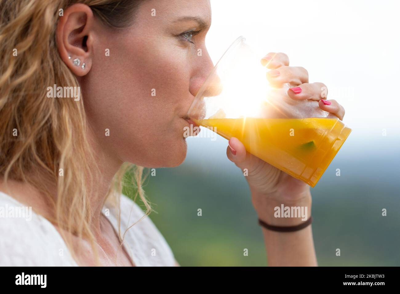 Young woman with curly hair drinking fresh juice at outdoors in sunrise, closeup, profile view Stock Photo
