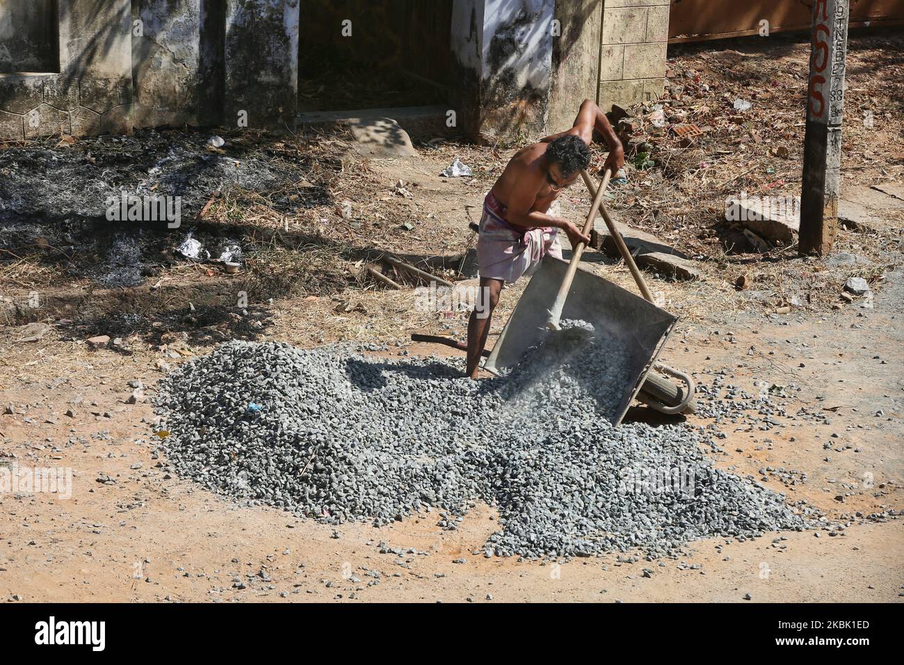 Labourer shoves gravel (to be used for construction) into a wheelbarrow