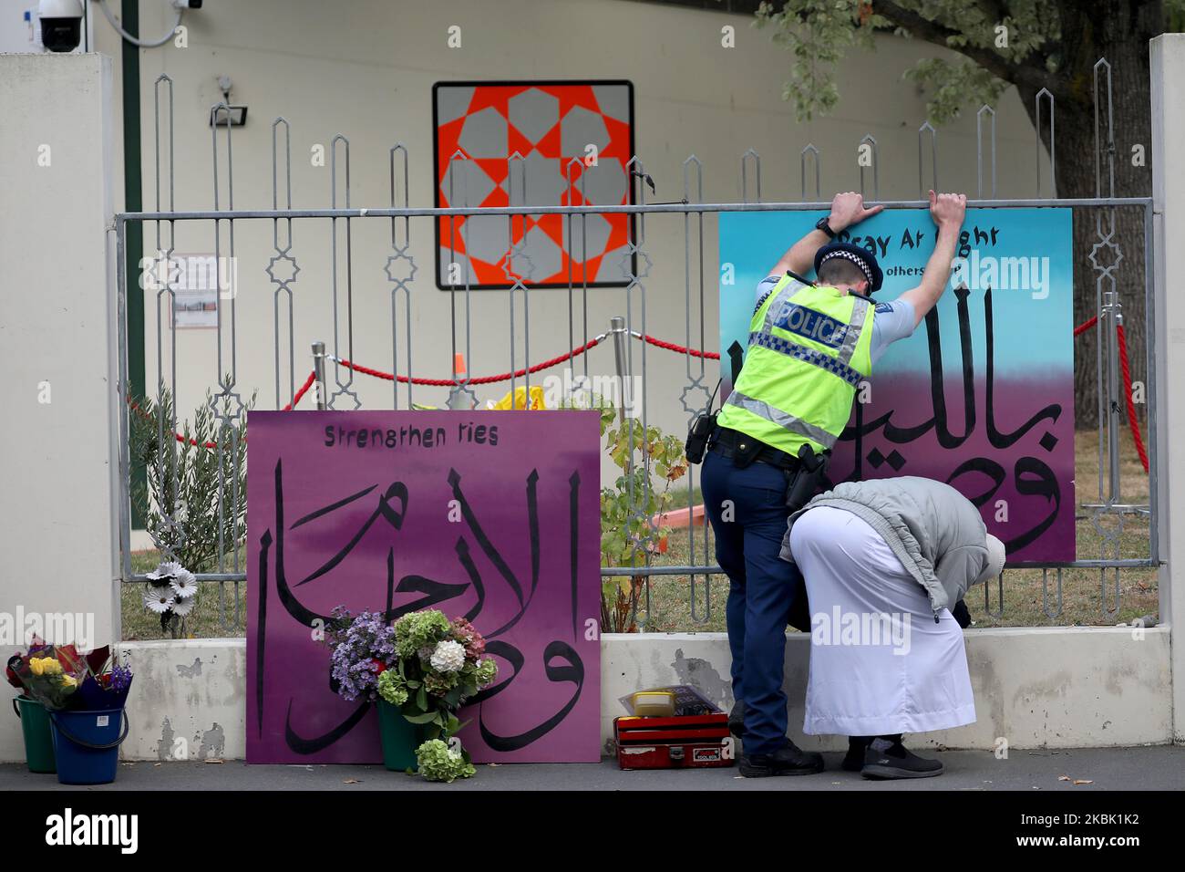 A police officer helps a member of the Muslim community to fix a bordÂ outside the Al Noor mosque in Christchurch, New Zealand on March 15, 2020. On March 15 last year, 51 people died and 49 were injured in the shootings at Christchurch's Al Noor and Linwood MosquesÂ when a gunman opened fire on worshippers.Â It was labeled as New Zealand's 'darkest day'.Â Events around the country including the Christchurch National Remembrance Service which marking the first anniversary of the attacks has been canceled amid safety fears over Covid-19.Â (Photo by Sanka Vidanagama/NurPhoto) Stock Photo