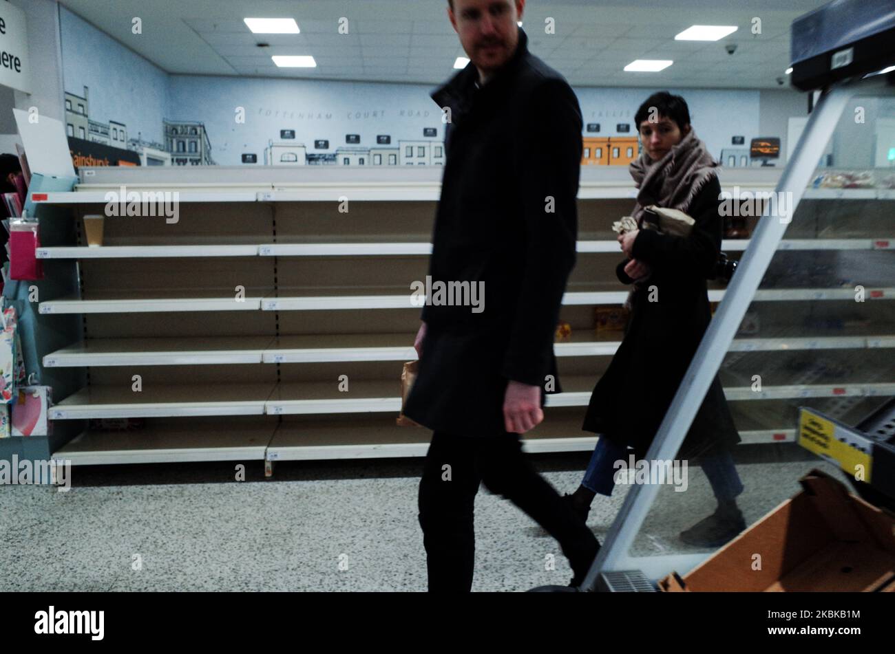 Shoppers walk past empty shelves, stripped through panic buying, in a branch of supermarket chain Sainsbury's on Tottenham Court Road in London, England, on March 21, 2020. Much of central London was virtually empty today, a day after British Prime Minister Boris Johnson ordered the closure of all pubs, bars, cafes and restaurants around the country. The move represents a toughening of measures to enforce the 'social distancing' that is being urged on citizens to reduce the growth of covid-19 coronavirus infections. Nightclubs, theatres, cinemas, gyms and leisure centres were also ordered clos Stock Photo