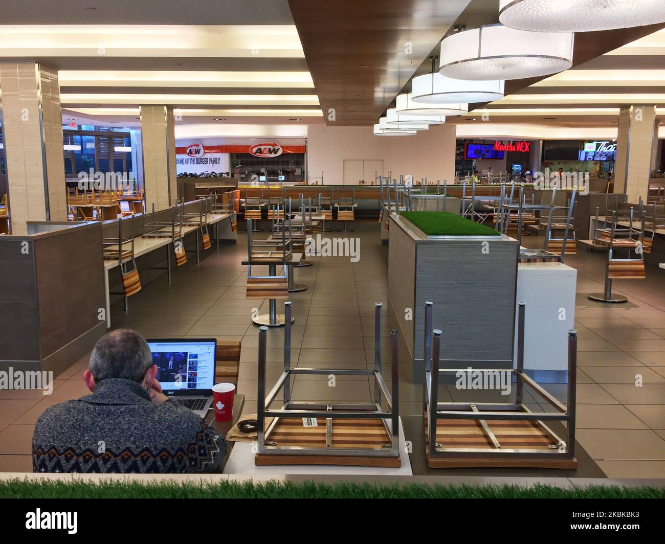 Lone man sits in an empty food court in a shopping mall in Toronto, Ontario, Canada on March 21, 2020. Restaurants have been prohibited from allowing dine-in service and food courts and cafeterias have been ordered to be closed by the Province of Ontario, with any deciding to remain open facing steep fines and penalties. Retailers in malls across Canada have shuttered their stores due to the novel coronavirus (COVID-19) outbreak. Many malls are limiting entry to only 50 visitors at a time. (Photo by Creative Touch Imaging Ltd./NurPhoto) Stock Photo