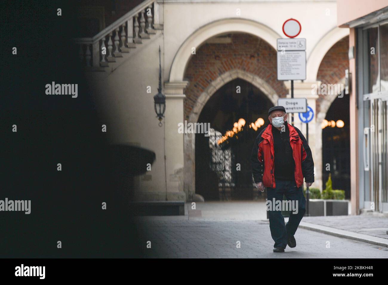 A man wearing a protective mask walks in an empty Krakow's Old Town. With 1,031 confirmed cases of coronavirus and 14 deaths, Poland's situation is deteriotating day by day. Polish PM Mateusz Morawiecki announced yesterday a series of new restrictions in the movement and contacts between people. The regulation concernes a ban on leaving the home except when necessary; going to work, grocery shops, doctors, pharmacies and walking dogs is allowed, as is a short walks and sports training alone and volunteers involved in the fight against the coronavirus. In addition, no more than two people shoul Stock Photo