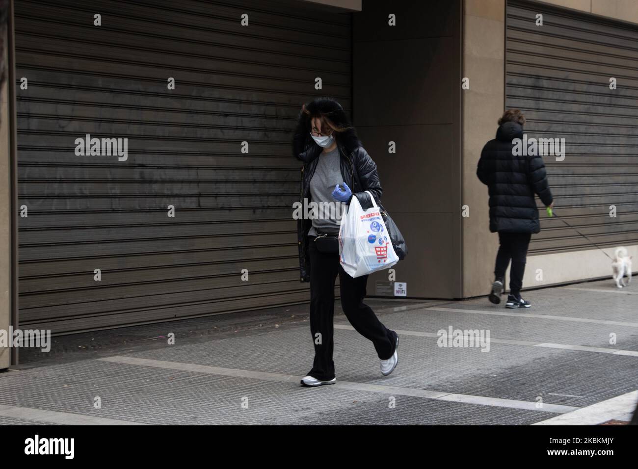 People as seen walking in front of sealed displays of closed shops because of the Coronavirus Covid-19 Pandemic outbreak with facemasks and protective gloves. Greece is in isolation from a big number of countries, closed land borders, ban in air flights connections and not accepting non EU citizens. People do social distancing because of the general quarantine in the country, public traffic ban and the total lockdown of the country since Monday 23 March 2020. All citizens who are outside of their houses are checked by the police for the special permission documents or SMS and ID that allows th Stock Photo