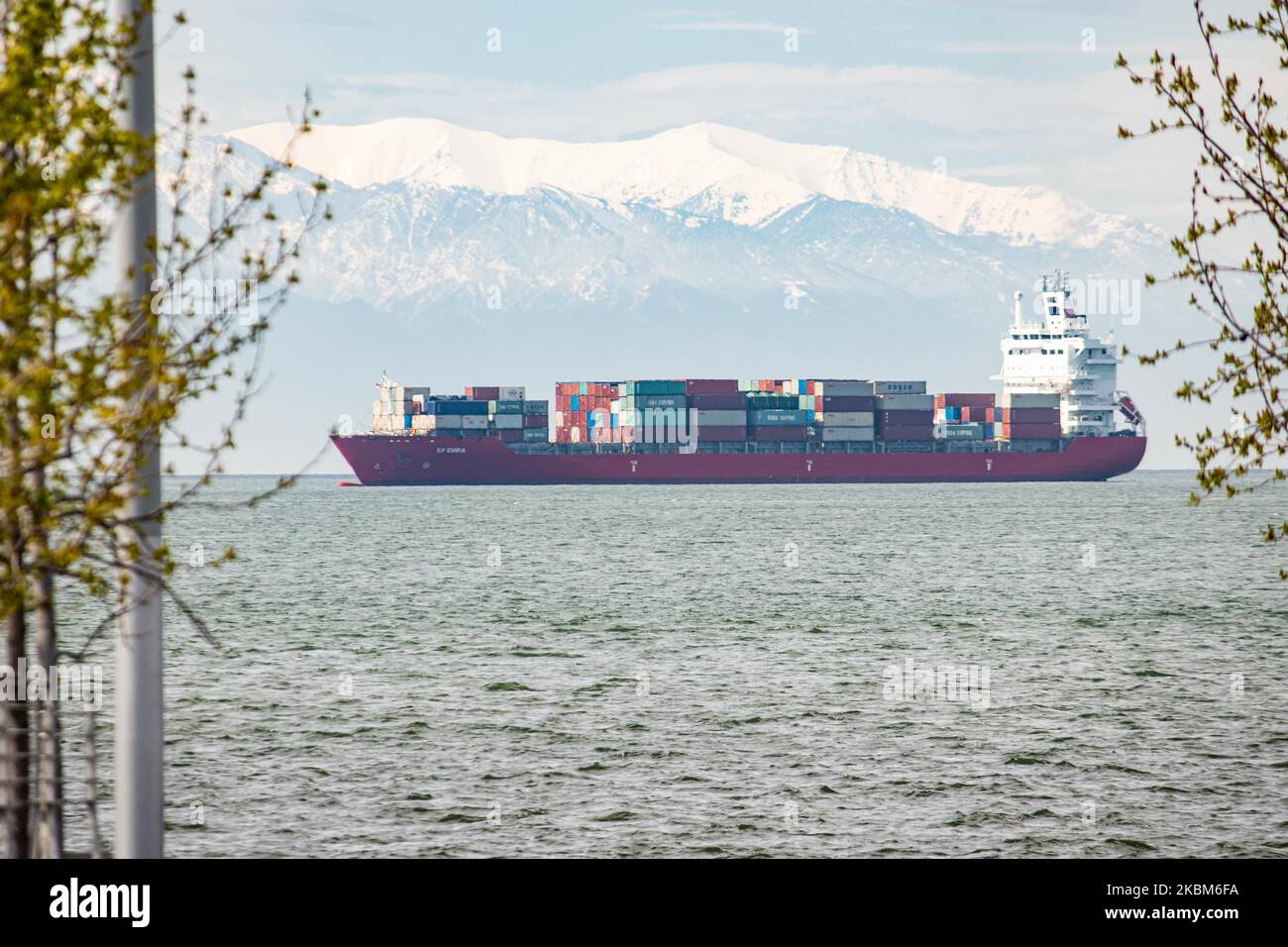 A freight vessel as seen from the seafront of Thessaloniki city anchored at Thermaikos Gulf, Aegean Sea in Greece on April 7, 2020. The cargo ship carries containers shipment and is under the name Ef Emira, with IMO registration number 9357810, sailing under the flag of Marshall Islands. The ship waits to unload its merchandise at the Port of Thessaloniki, the second-largest container port in Greece but there is a delay in the port due to Covid-19 Coronavirus Pandemic. Snow covered Mount Olympus is visible in the background. (Photo by Nicolas Economou/NurPhoto) Stock Photo