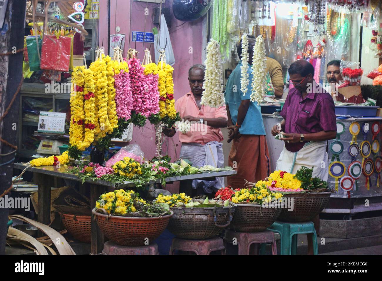 Flower sellers make garlands of jasmine flowers at a flower market in