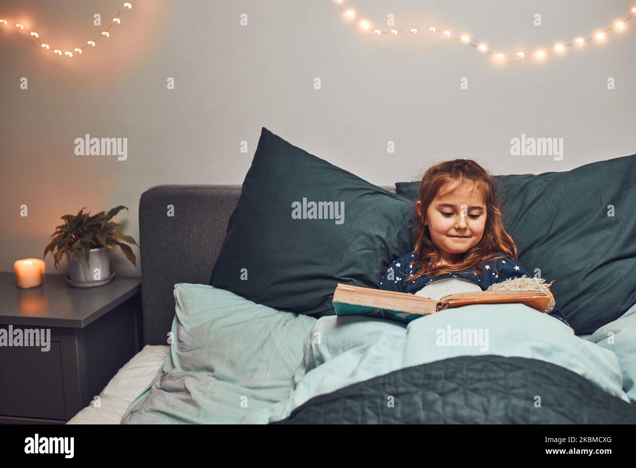 Little girl reading book and watching pictures in bed before going to