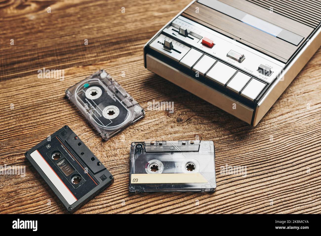 Compact cassette tapes and cassette recorder on wooden table. Retro
