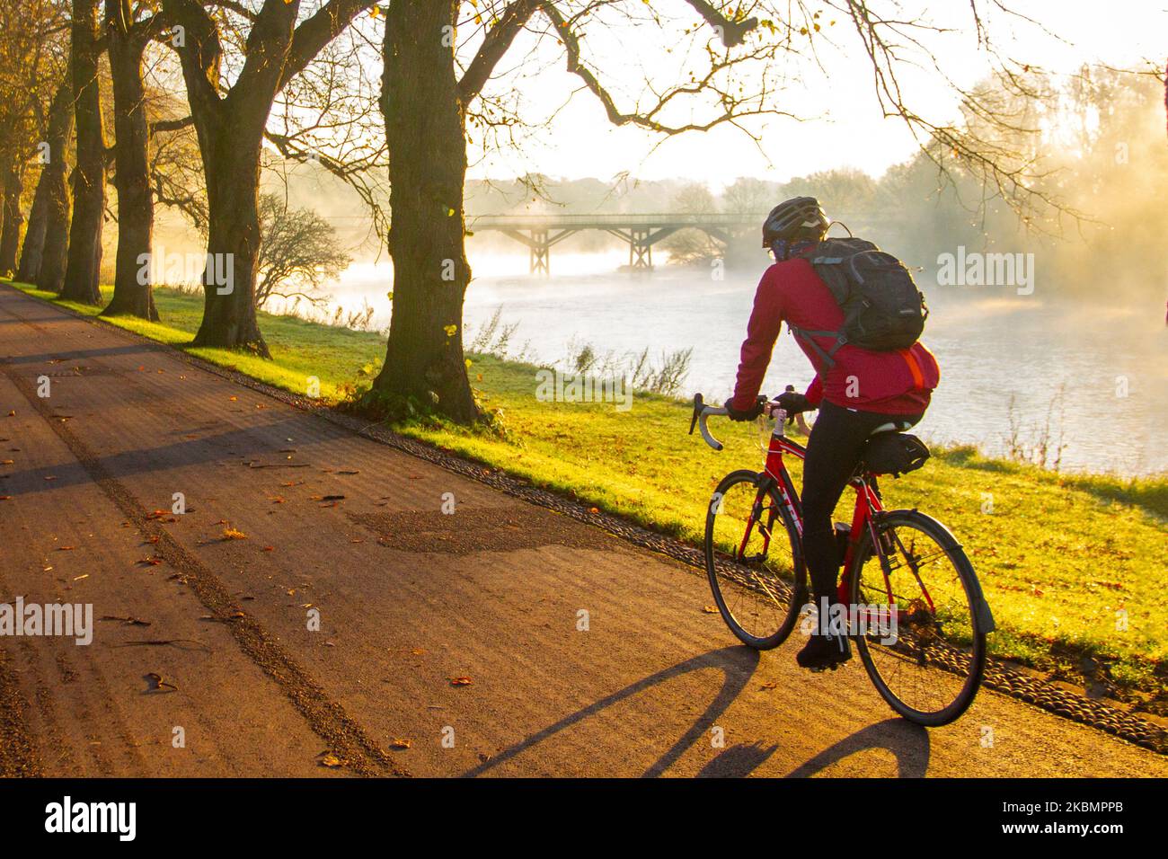 Cyclist riding alongside the River Ribble as the sun rises on a mist day in Preston, Lancashire. UK Weather 4 November, 2022.  Cold frosty, misty morning as the sun rises over the River Ribble and local residents take light exercise along the riverside walk in Avenham Park. Sunny spells after the first frost of Autumn.  Credit; MediaWorldImages/AlamyLiveNews Stock Photo